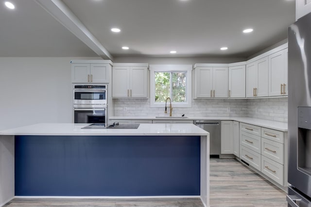 kitchen featuring appliances with stainless steel finishes, a sink, light wood-style floors, backsplash, and recessed lighting