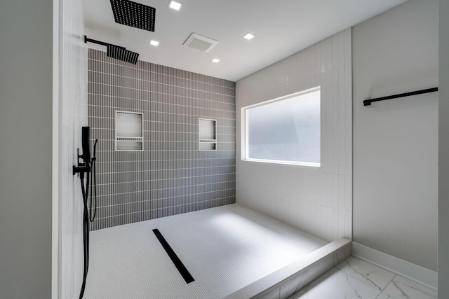 bathroom featuring marble finish floor, a tile shower, and baseboards