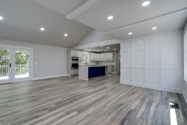 unfurnished living room with light wood-type flooring, lofted ceiling, a decorative wall, and baseboards