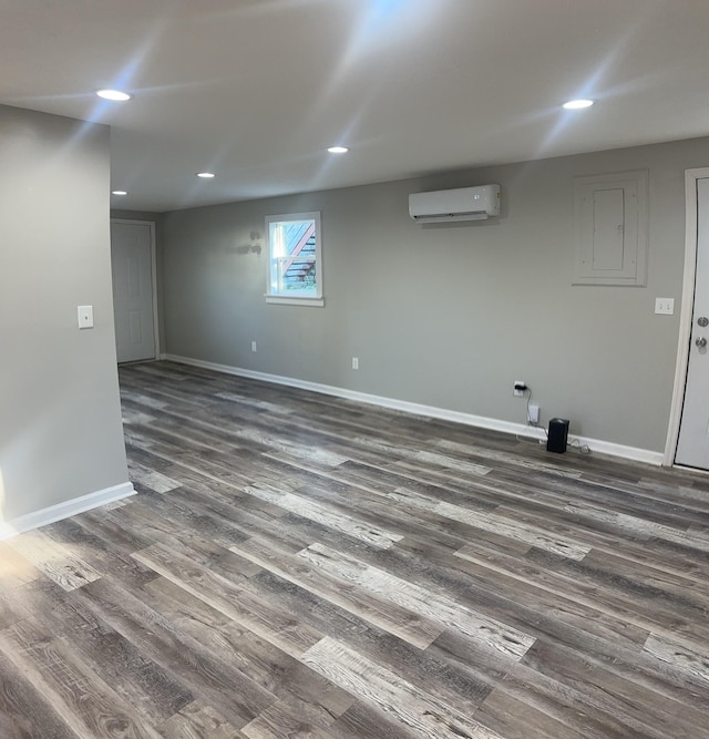 basement with electric panel, baseboards, a wall unit AC, dark wood-style flooring, and recessed lighting