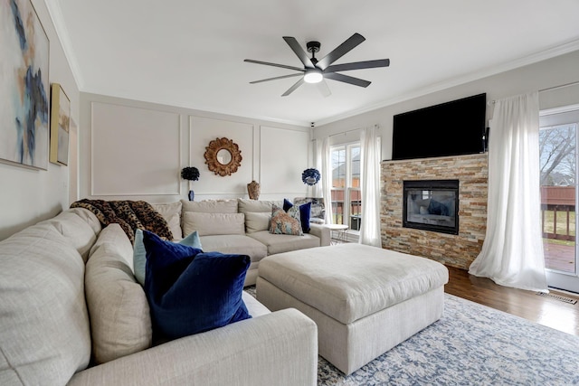 living room with visible vents, ornamental molding, wood finished floors, a stone fireplace, and a decorative wall