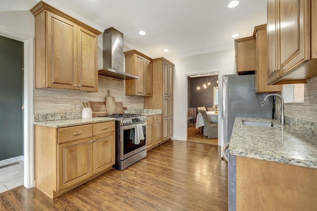 kitchen featuring ornamental molding, stainless steel gas stove, a sink, wall chimney range hood, and wood finished floors