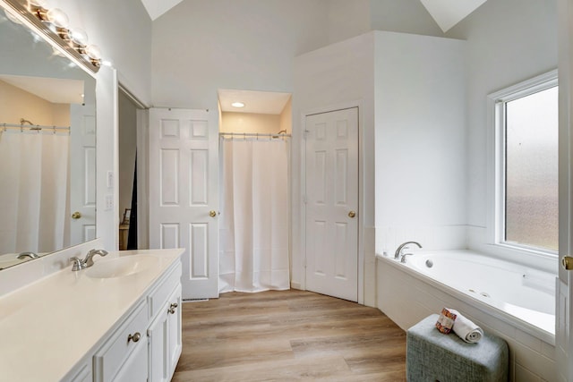 bathroom with lofted ceiling, a garden tub, wood finished floors, and vanity