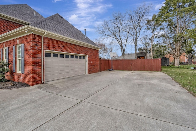 view of side of property featuring a shingled roof, concrete driveway, brick siding, and fence