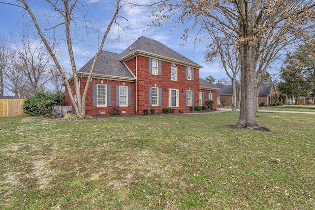 colonial house with brick siding, a shingled roof, fence, crawl space, and a front yard