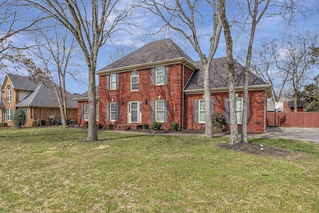 colonial home featuring a front yard, brick siding, fence, and roof with shingles