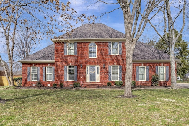 colonial home with a shingled roof, a front yard, and brick siding