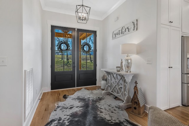 entryway with baseboards, french doors, ornamental molding, light wood-type flooring, and an inviting chandelier