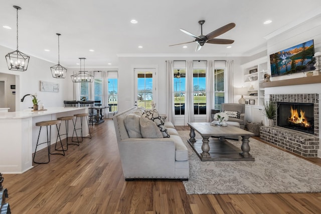 living room with built in shelves, recessed lighting, ornamental molding, a brick fireplace, and wood finished floors