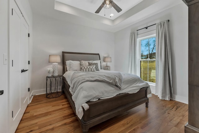 bedroom featuring a ceiling fan, baseboards, a raised ceiling, and wood finished floors