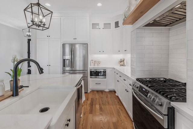 kitchen with tasteful backsplash, wall chimney exhaust hood, stainless steel appliances, light wood-type flooring, and a sink