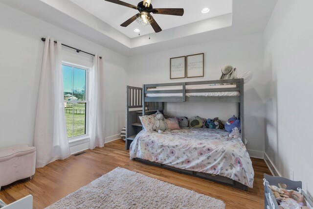 bedroom featuring a tray ceiling, wood finished floors, and baseboards