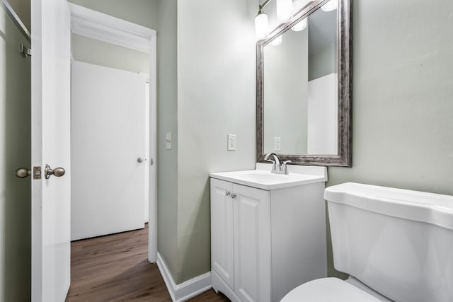 half bath with wood finished floors, vanity, toilet, and baseboards