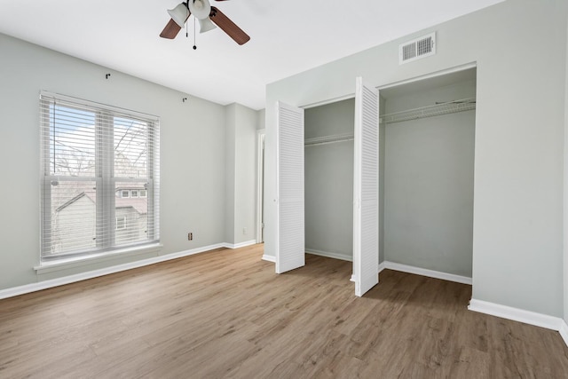 unfurnished bedroom with two closets, visible vents, ceiling fan, wood finished floors, and baseboards