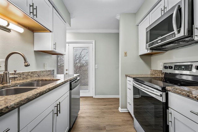 kitchen featuring light wood finished floors, stone countertops, appliances with stainless steel finishes, crown molding, and a sink