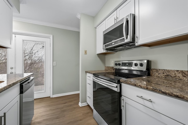 kitchen with ornamental molding, dark stone countertops, stainless steel appliances, light wood-type flooring, and white cabinetry