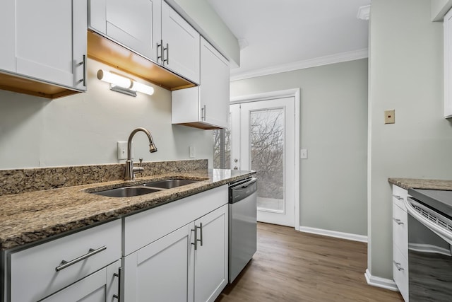 kitchen with stainless steel appliances, ornamental molding, white cabinetry, a sink, and dark stone countertops