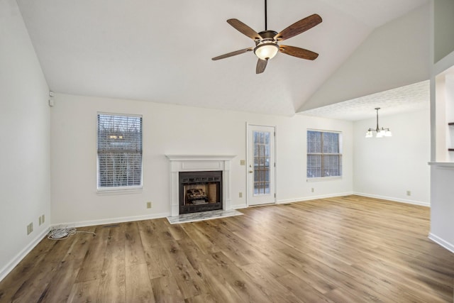 unfurnished living room with baseboards, wood finished floors, vaulted ceiling, a fireplace, and ceiling fan with notable chandelier