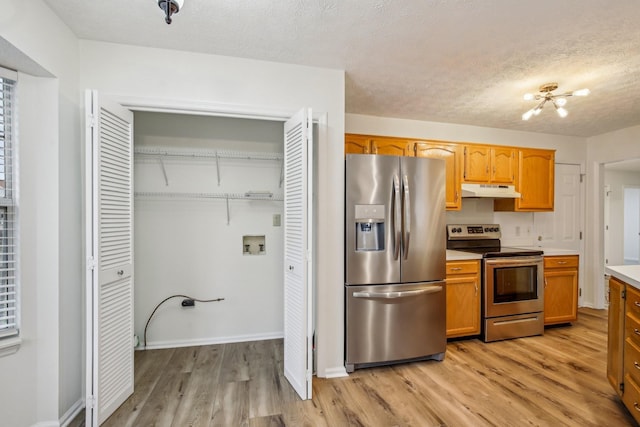 kitchen with light wood finished floors, appliances with stainless steel finishes, light countertops, a textured ceiling, and under cabinet range hood