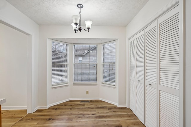 unfurnished dining area featuring a textured ceiling, light wood-type flooring, and a notable chandelier