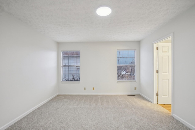 unfurnished room with light carpet, visible vents, baseboards, and a textured ceiling