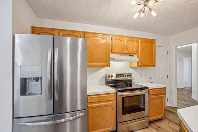 kitchen featuring light countertops, light wood-style flooring, appliances with stainless steel finishes, a textured ceiling, and under cabinet range hood