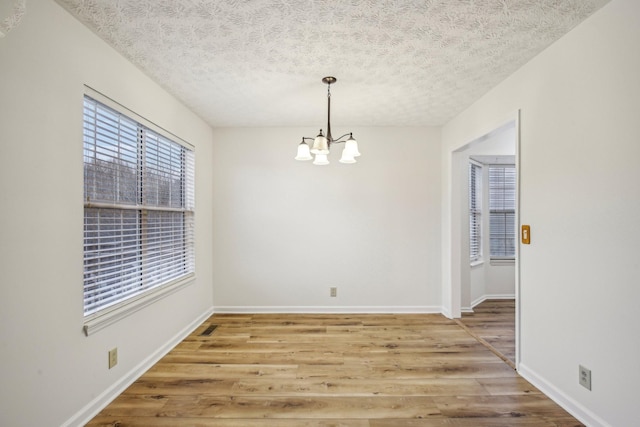 unfurnished dining area with a chandelier, a textured ceiling, light wood-style flooring, and baseboards