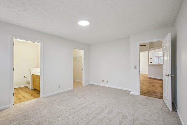 unfurnished bedroom featuring ensuite bath, baseboards, a walk in closet, and light colored carpet