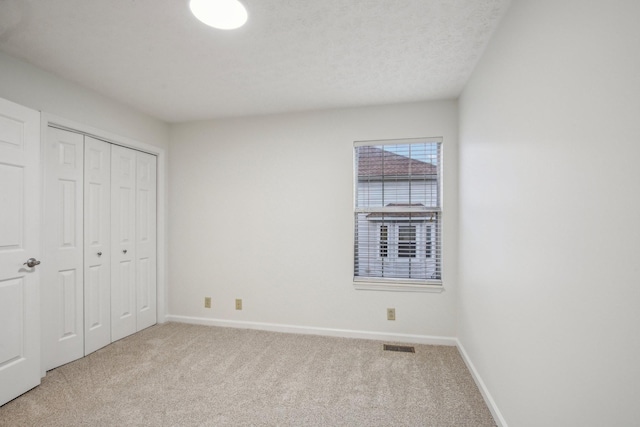 unfurnished bedroom featuring light carpet, visible vents, baseboards, a textured ceiling, and a closet