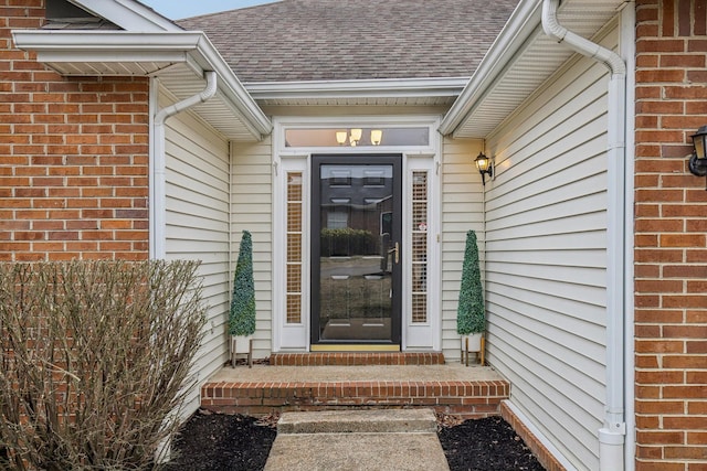 view of exterior entry with brick siding and roof with shingles