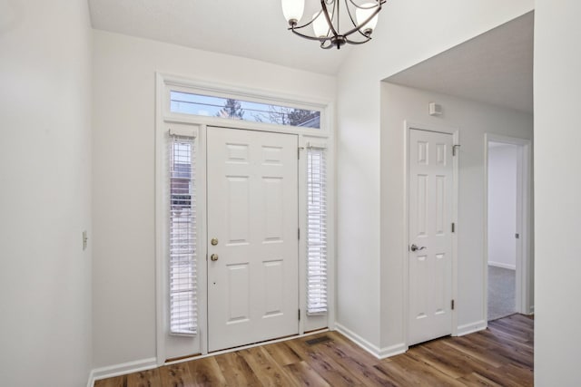 entryway with a chandelier, wood finished floors, lofted ceiling, and baseboards