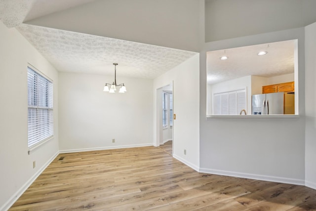 spare room featuring a textured ceiling, recessed lighting, a notable chandelier, baseboards, and light wood-style floors