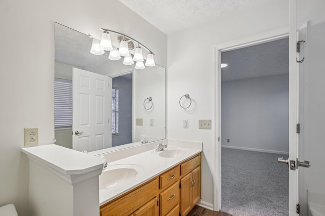 full bathroom with a textured ceiling, double vanity, a sink, and baseboards