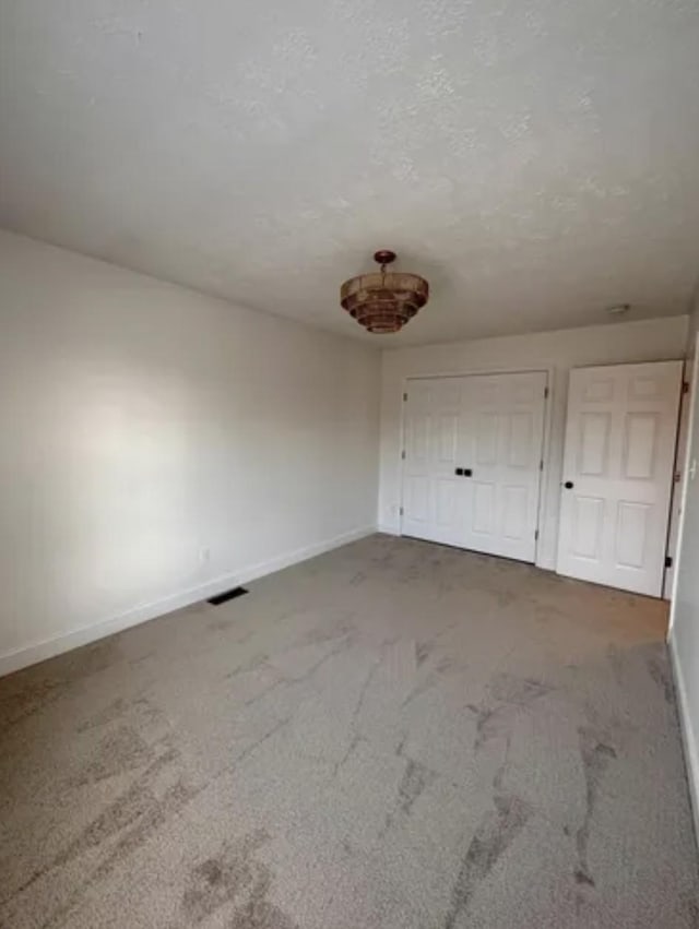 unfurnished bedroom with baseboards, visible vents, a textured ceiling, carpet floors, and a closet