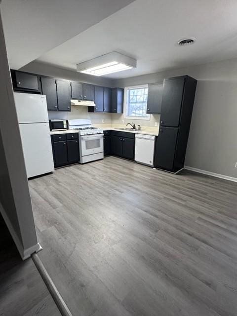 kitchen with light countertops, light wood-style floors, white appliances, under cabinet range hood, and baseboards