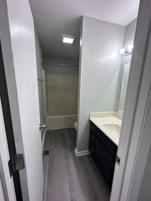 bathroom featuring toilet, tub / shower combination, vanity, wood finished floors, and baseboards