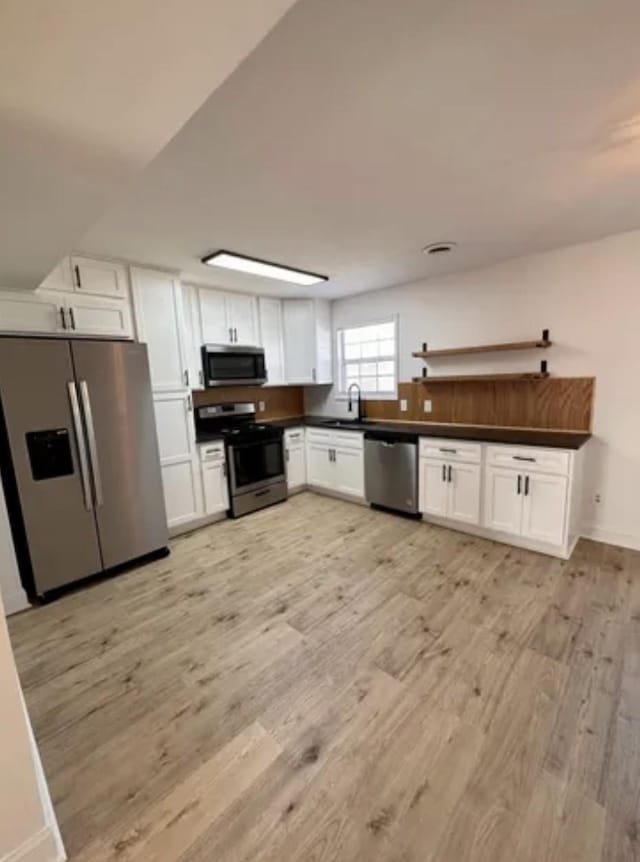 kitchen featuring appliances with stainless steel finishes, dark countertops, light wood-type flooring, and white cabinets