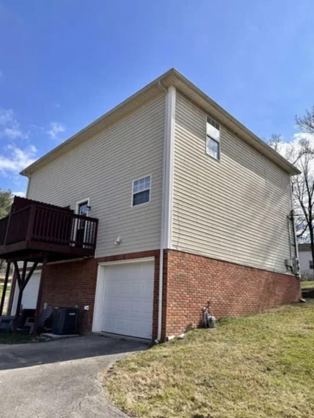 view of property exterior with aphalt driveway, brick siding, an attached garage, central AC, and a deck