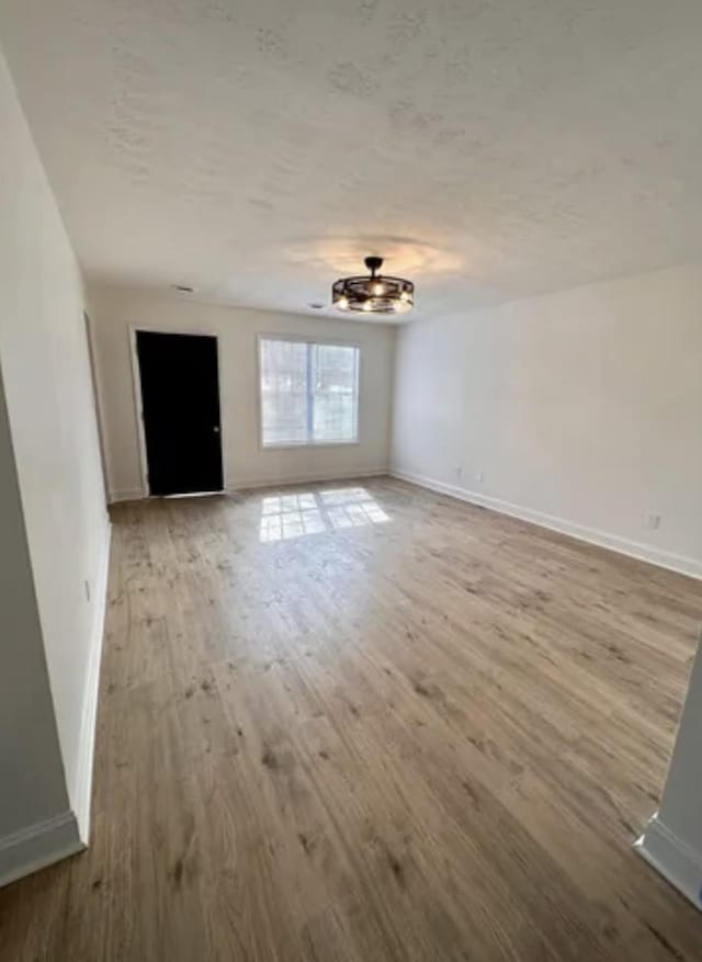 unfurnished living room with a textured ceiling, baseboards, and wood finished floors