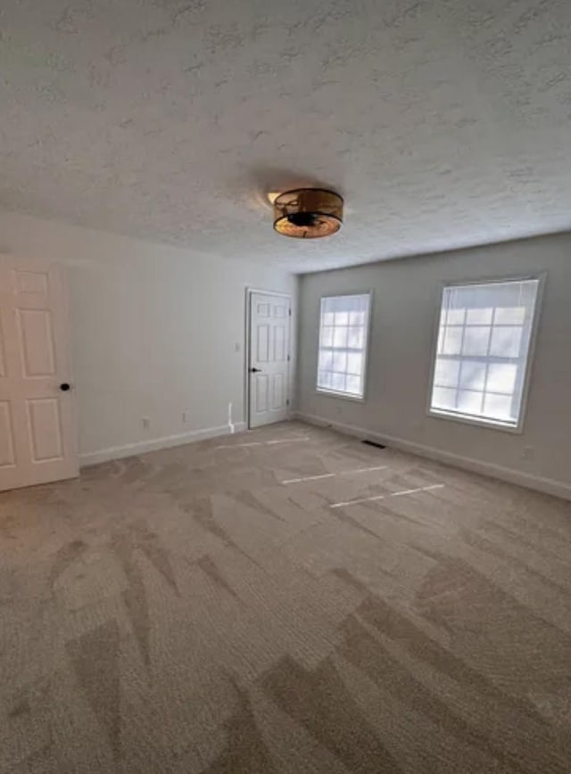 spare room with light carpet, visible vents, baseboards, and a textured ceiling