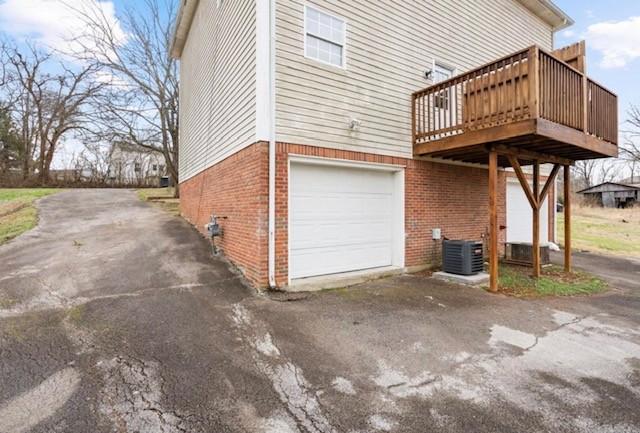 view of property exterior with an attached garage, central AC unit, a deck, and brick siding