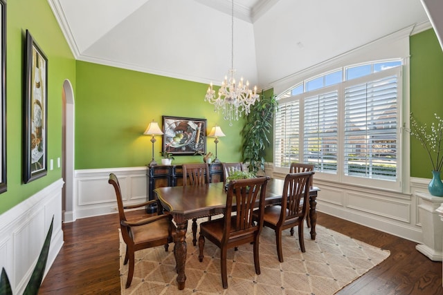 dining space featuring wood finished floors, a wainscoted wall, an inviting chandelier, vaulted ceiling, and crown molding