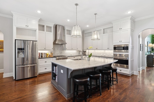 kitchen featuring arched walkways, dark wood-style flooring, a sink, stainless steel appliances, and wall chimney exhaust hood