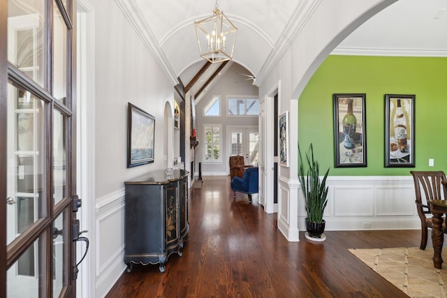 entryway featuring a notable chandelier, ornamental molding, wood finished floors, arched walkways, and vaulted ceiling