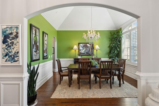 dining room with wood finished floors, a wainscoted wall, an inviting chandelier, lofted ceiling, and arched walkways