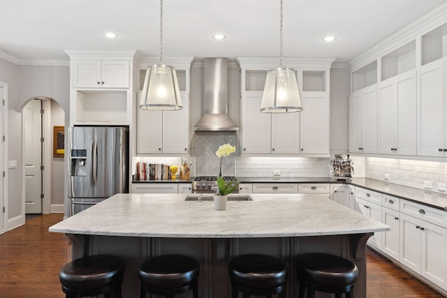 kitchen with stainless steel fridge, arched walkways, a breakfast bar area, and wall chimney range hood