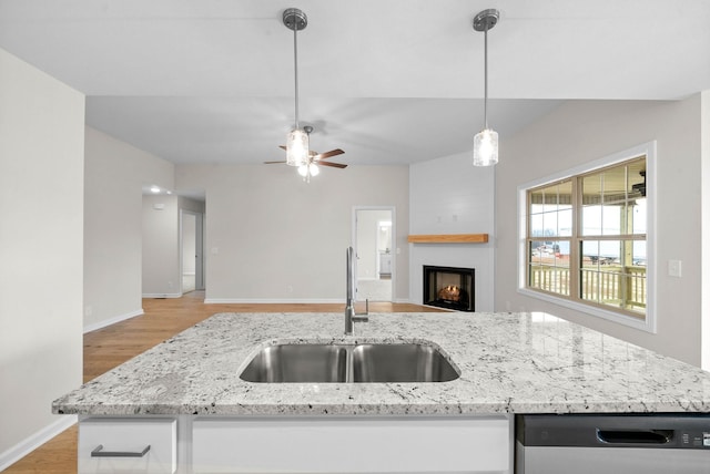 kitchen featuring a fireplace, a sink, open floor plan, stainless steel dishwasher, and light stone countertops