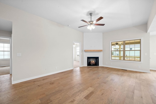 unfurnished living room featuring a lit fireplace, visible vents, ceiling fan, and light wood-style flooring