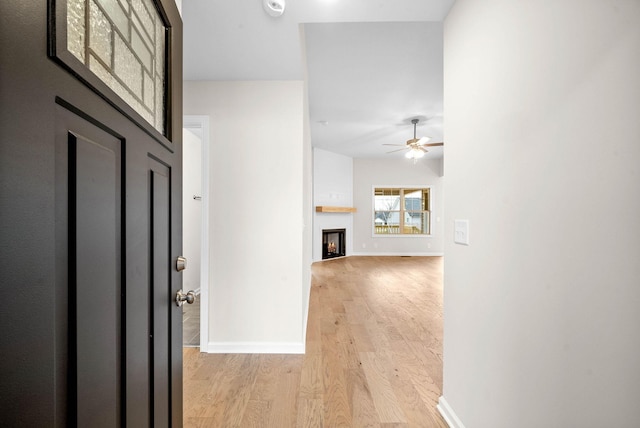 entryway with light wood-style floors, a warm lit fireplace, baseboards, and a ceiling fan