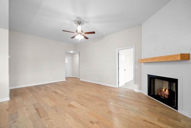 unfurnished living room featuring a large fireplace, ceiling fan, baseboards, and light wood-style floors